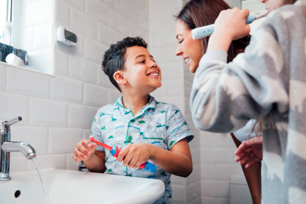 DrDalmao-Children are brushing their teeth in the bathroom at home. The mother is checking the little boy's mouth to make sure he has brushed properly.
